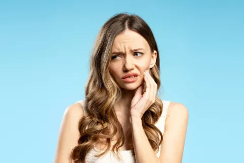 Dolor de muelas por caries tras despertar una lesión inactiva Mujer con pelo largo se lleva la mano a la mandíbula por dolor de muelas