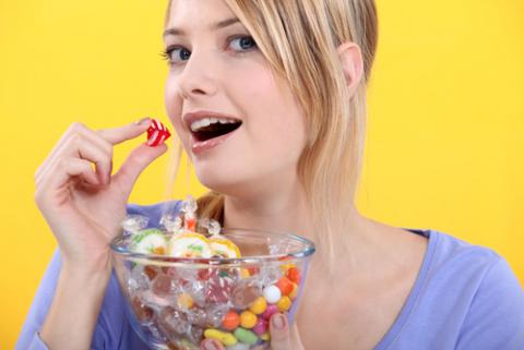 Una mujer sostiene un bol lleno de caramelos, a punto de comerse uno