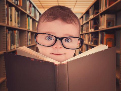 Un bebé con gafas frente a un libro abierto