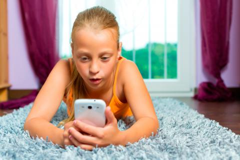 Una niña consulta su smartphone tumbada en su cama