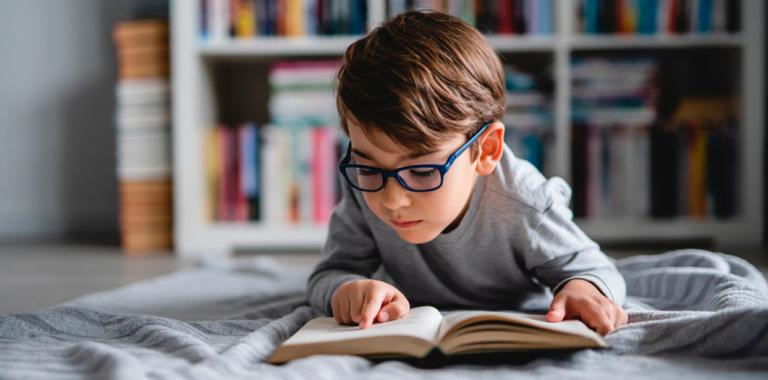 Un niño con gafas tendido en el suelo y leyendo un libro