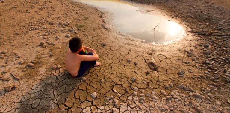 Niño sentado en tierra agrietada junto a una laguna seca