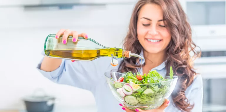 Mujer echando aceite de oliva a una ensalada