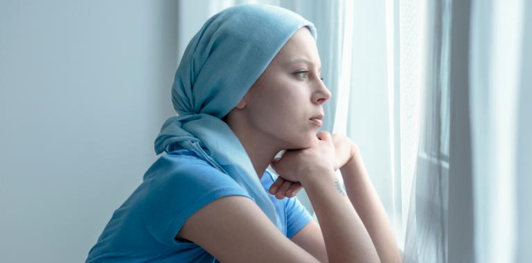 Mujer enferma de cáncer con la mirada perdida frente a una ventana 