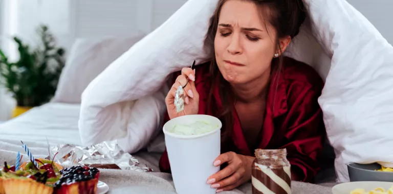 Mujer en la cama comiendo ultraprocesados