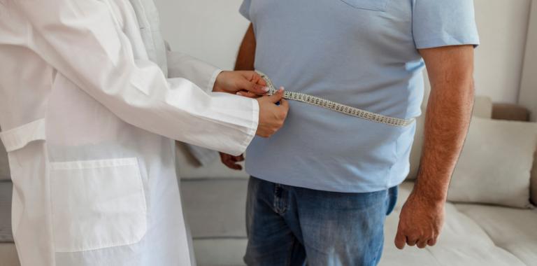 Doctor midiendo el perímetro abdominal a un hombre de mediana edad