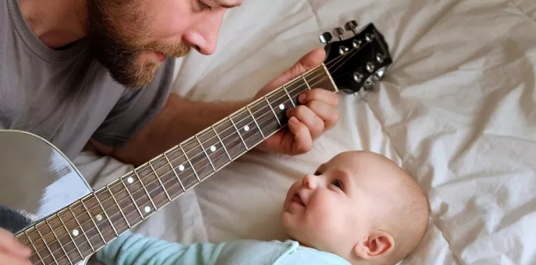 Padre toca la guitarra para su bebé en la cama