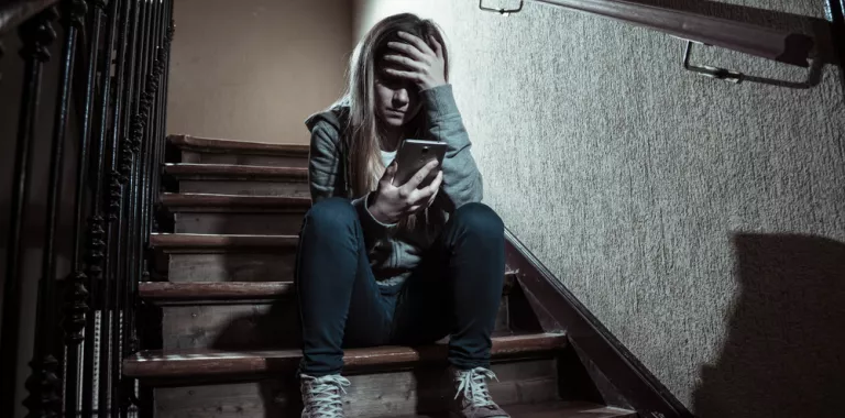 Niña adolescente sentada en la escalera de un edificio mirando su móvil con gesto de preocupación