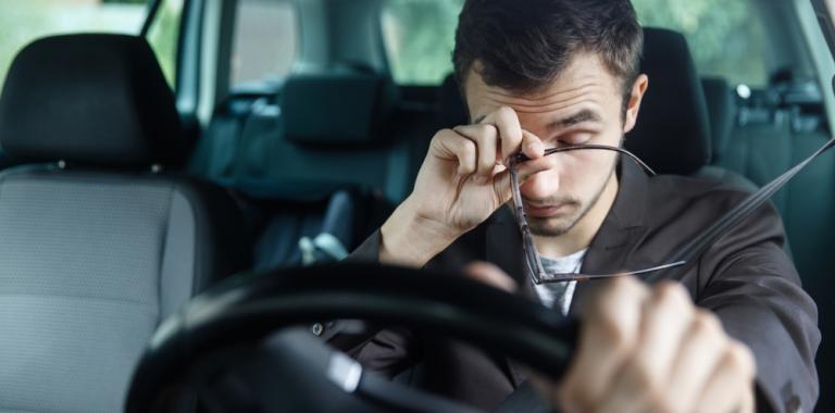 Un hombre frotándose los ojos mientras conduce