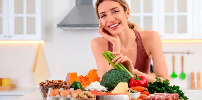 Mujer sonriendo y sentada en una mesa con alimentos sanos