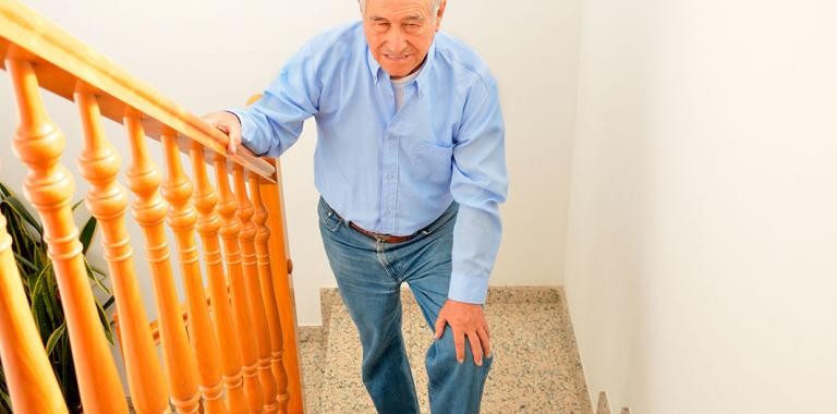 Hombre mayor se toca la rodilla dolorida al subir una escalera