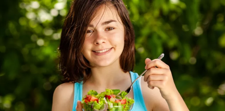 Una niña sonríe mientras se dispone a comerse una ensalada