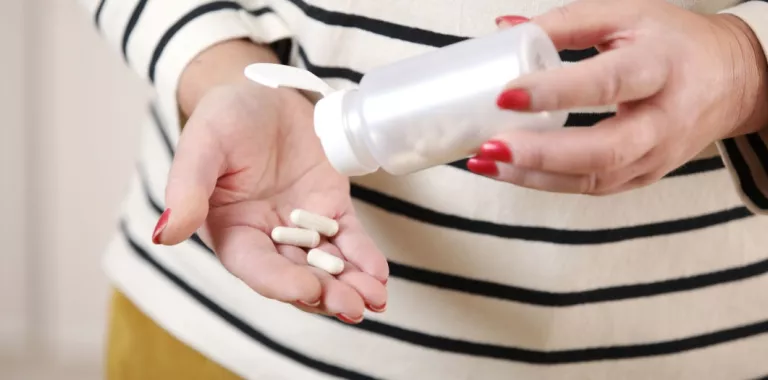 Mano de mujer con unas píldoras que han salido de un bote abierto en su otra mano