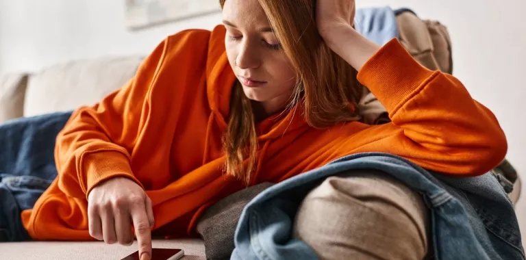 Adolescente triste mirando su smartphone desde el sofá