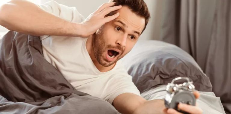 Hombre en la cama se asusta al comprobar en su despertador que ya es muy tarde