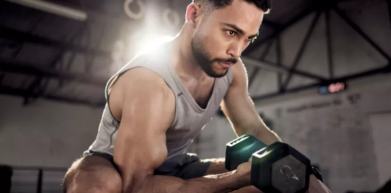 Hombre joven musculado entrena con mancuernas en un gimnasio