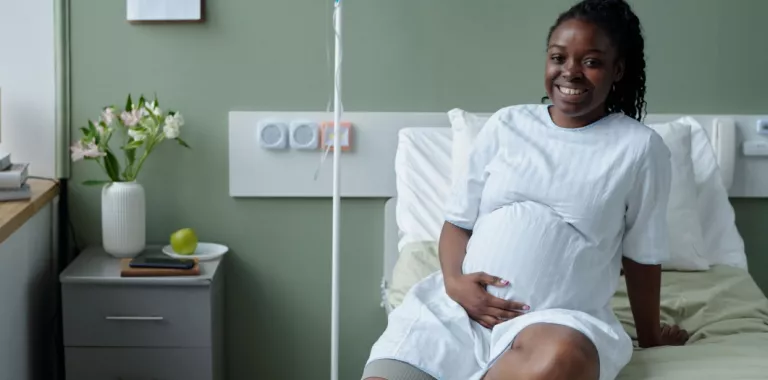 Sonriente joven negra embarazada sentada sobre la cama del hospital
