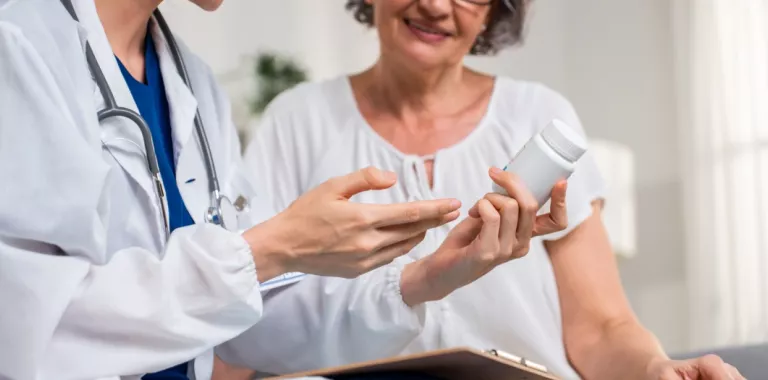 Doctora muestra frasco pastillas a una mujer mayor