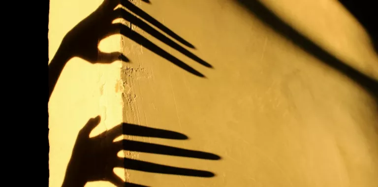 Sombra alargada de dos manos sobre una pared amarilla