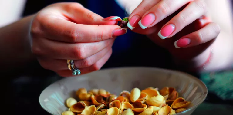 Manos de mujer con uñas pintadas pelan pistachos