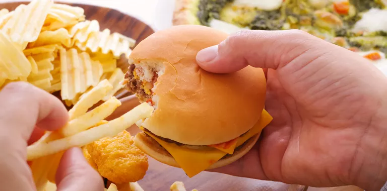 Manos sostienen una hamburguesa y unas patatas fritas