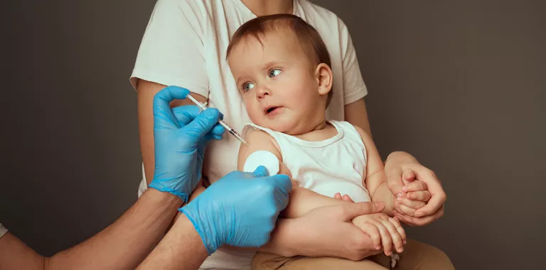 Cuidador sostiene a un niño pequeño en preparación para una vacunación
