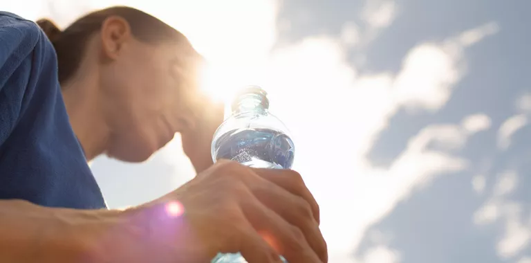 Mujer que bebe el agua que se refresca en la onda de calor extrema