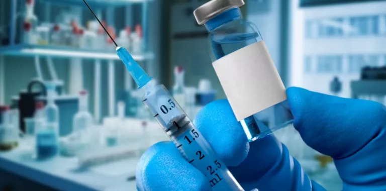 Mano de un investigador sostiene un vial de vacuna experimental y una jeringuilla