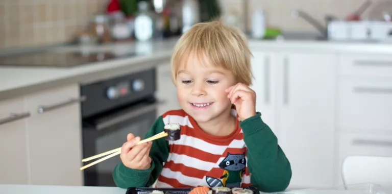Un niño sonriente se dispone a comer un plato de sushi en la cocina de su casa