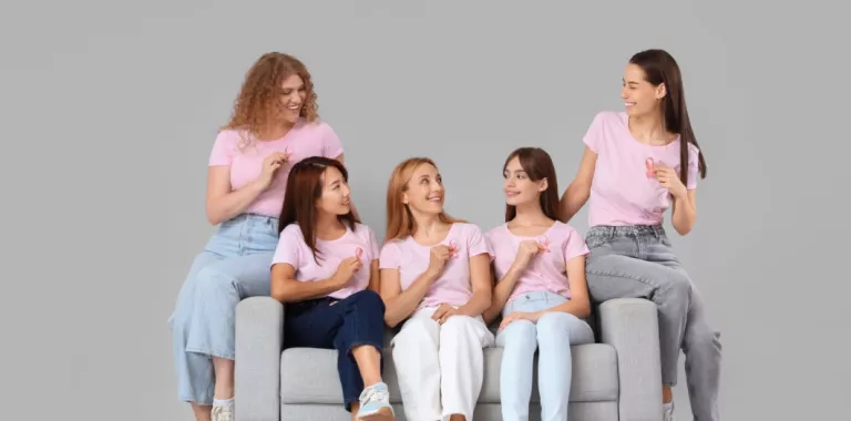 Grupo de mujeres jóvenes con cintas rosadas contra el cáncer de mama sentadas en un sofá