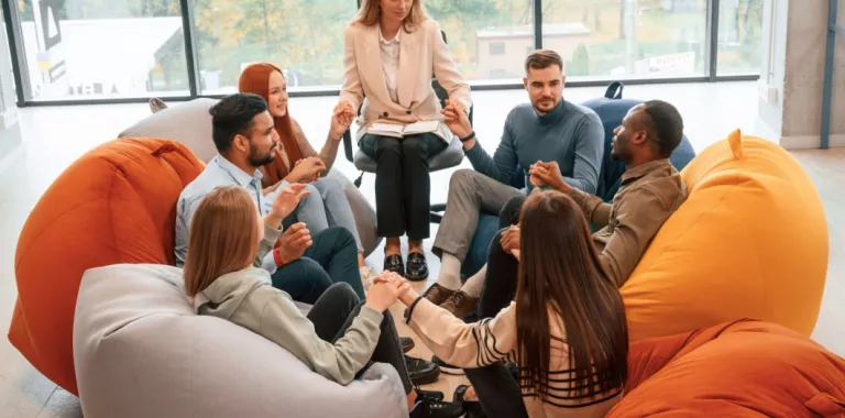 Grupo de jóvenes sentados en círculo alrededor de su terapeuta cogidos de la mano