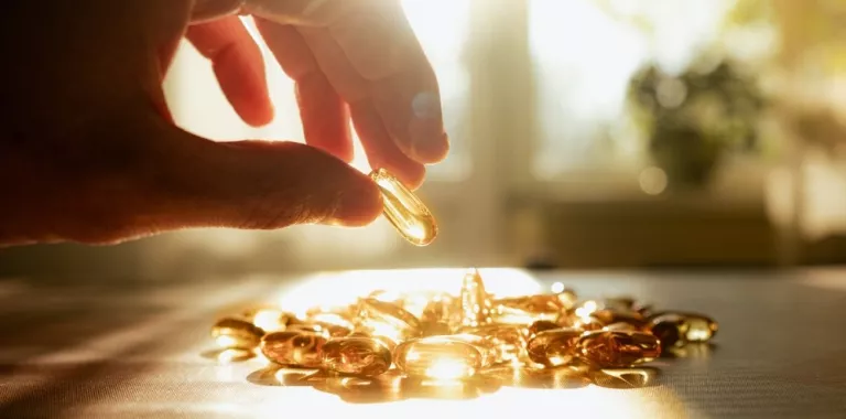 Una mano cogiendo suplementos de vitamina D iluminados por el sol