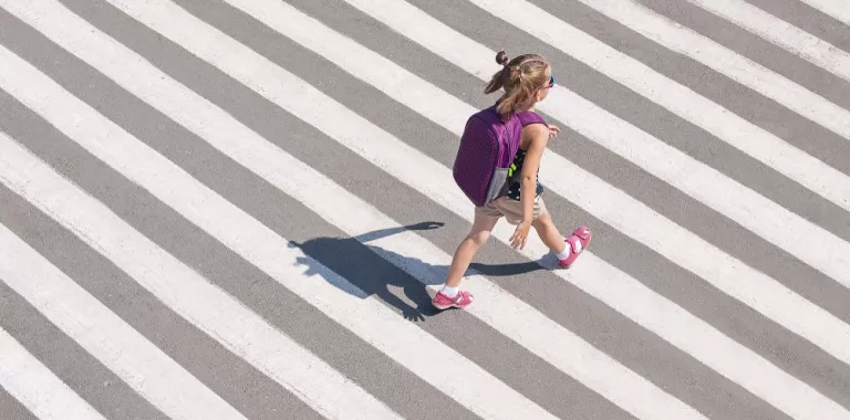 Niña va al colegio con mochila caminando atravesando un paso de cebra
