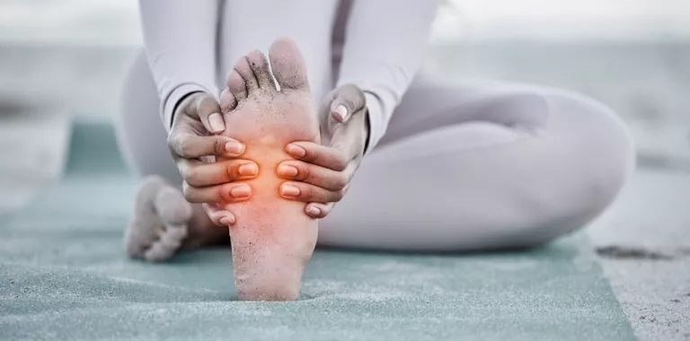 Mujer se duele de un pie sentada sobre una esterilla