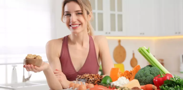Mujer joven sonríe en su cocina junto a alimentos saludables