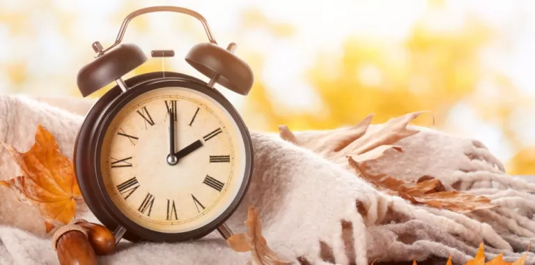 Reloj despertador junto a manta y hojas otoñales