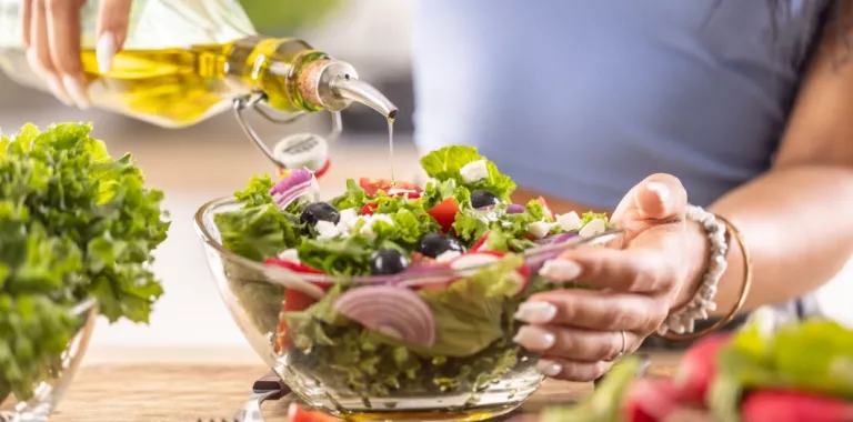 Una mujer aliña una ensalada de estilo mediterráneo con aceite de oliva