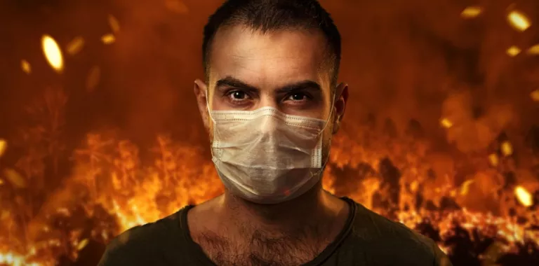 Hombre se protege con una máscara con un incendio forestal a su espalda