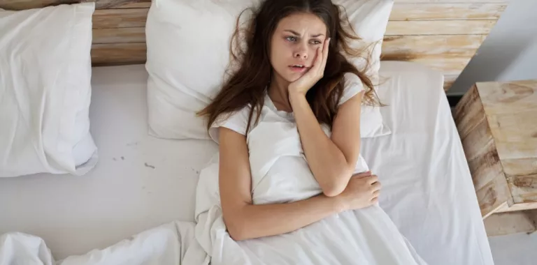 Mujer joven tumbada en la cama con gesto preocupado