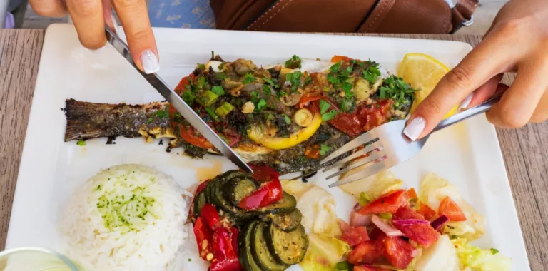 Pescado y verduras típicos de la dieta mediterránea listos para comer Manos de mujer cortan alimentos de un menú típico de la dieta mediterránea