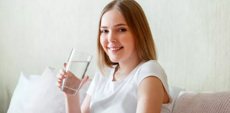 Chica joven sonríe a la cámara sosteniendo un vaso de agua