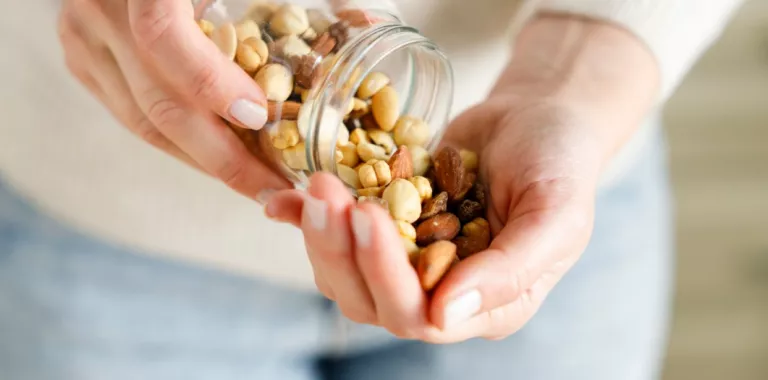 Mujer vuelca un puñado de frutos secos en su mano Manos de mujer sostienen un tarro de cristal con frutos secos