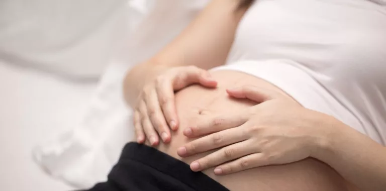 Embarazada recostada con las manos sobre el vientre