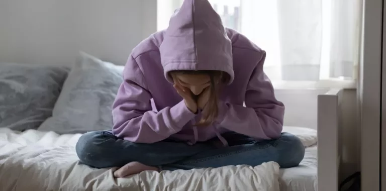 Niña adolescente triste sentada en la cama oculta su cara con las manos