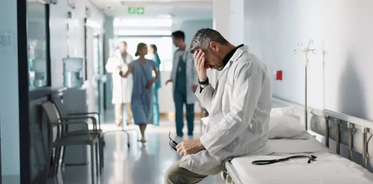 Médico sentado sobre una camilla se toca la frente con gesto abatido
