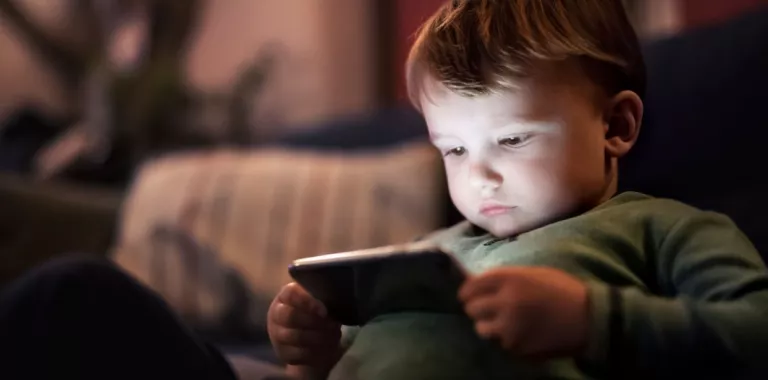 Niño pequeño sentado en la cama mirando un móvil