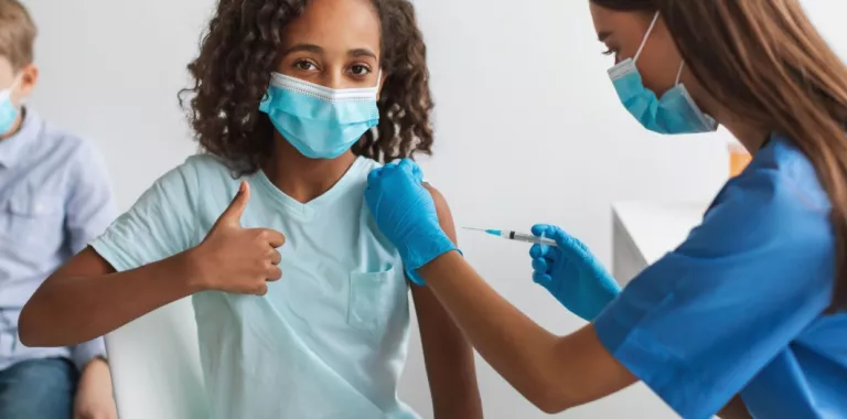 Sanitaria vacunando a una niña contra el COVID-19 Niña hace un gesto de aprobación con el pulgar mientras es vacunada