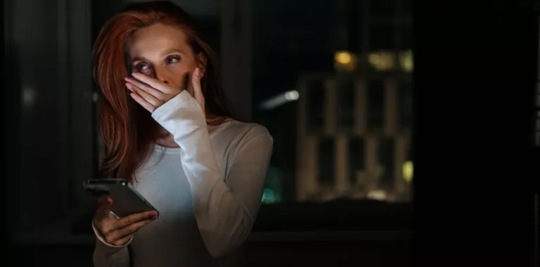 Mujer en una habitación a oscuras bosteza con el móvil en la mano