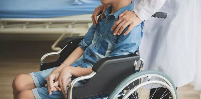 Niño en silla de ruedas con distrofia muscular atendido por un médico Médico apoya sus manos sobre un niño en silla de ruedas con problemas musculares