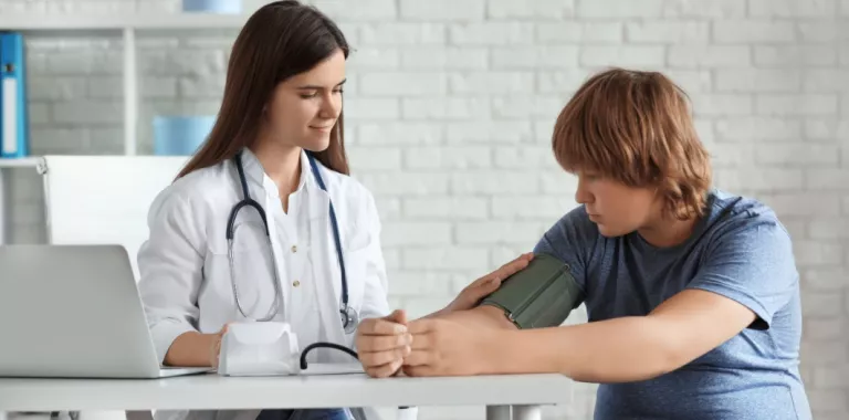 Doctora mide la presión arterial de un adolescente con sobrepeso Doctora toma la tensión arterial a un adolescente
